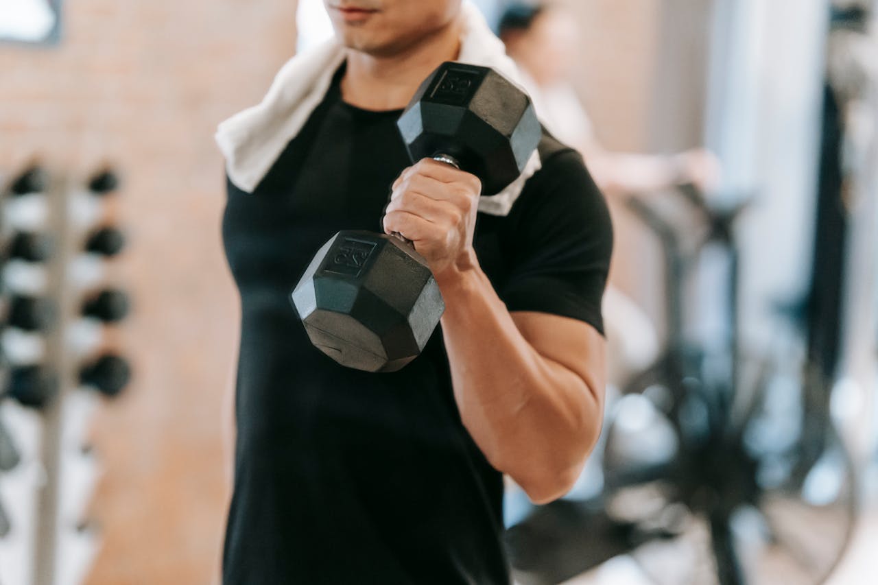Home Unrecognizable strong male with towel wearing black activewear lifting heavy dumbbell during intense training in fitness studio with special equipment on blurred background